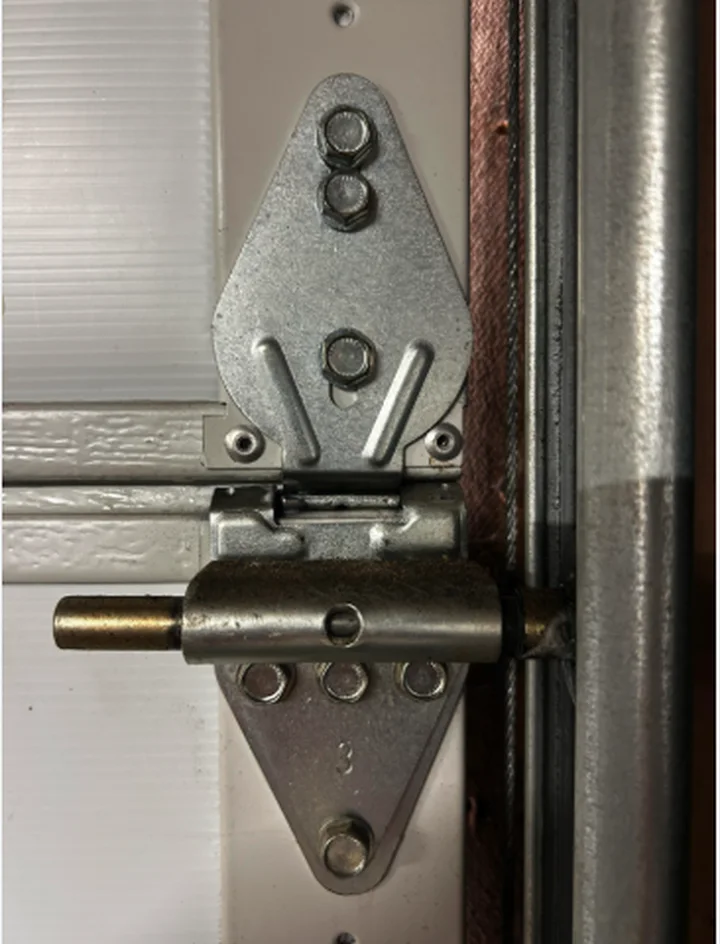 Galvanised garage door hinge bolted to a white door section with the roller in the track